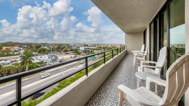 A balcony with a view of a busy road and buildings, featuring a tiled floor and white chairs. - Anchorage Resort 8th Floor Condo in Siesta Key With Private Beach Access, Pool, Boat Dock 0894 (Siesta Key)