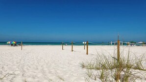 Une plage avec un filet de volley-ball, un parasol coloré et un ciel bleu azur.