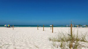 A beach with a volleyball net, a colorful umbrella, and a clear blue sky.