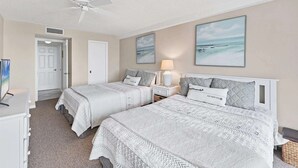 Une chambre d’hôtel avec deux lits, un ventilateur de plafond, une télévision et des œuvres d’art accrochées aux murs.