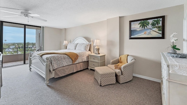 Une chambre à coucher comprenant un lit, des tables de chevet, une chaise, une commode, un tableau et une vue sur l’extérieur, visible à travers une porte-fenêtre donnant sur un balcon.