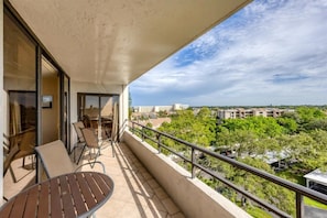 A balcony with a table and chairs, a sliding glass door, and a view of buildings and trees. - Anchorage Resort 7th Floor 2-bedroom Condo w Private Balcony Beach Access 0893 (Siesta Key)