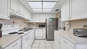 A modern kitchen with white cabinets, a stainless steel refrigerator, a microwave, a stove, and a toaster. - Anchorage Resort 3rd Floor 2 Bedroom Condo South West Balconies 0885 (Siesta Key)