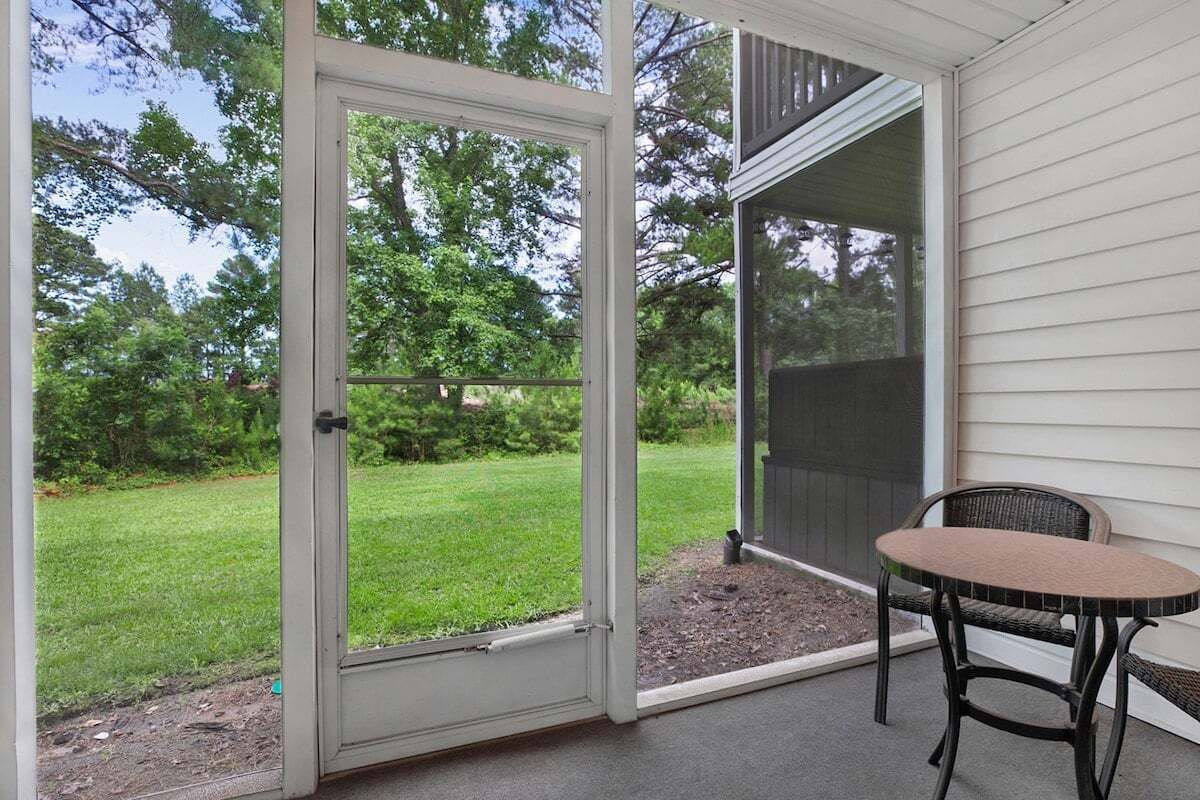 A covered patio with a sliding glass door leading to a grassy yard, a round table, and a chair.