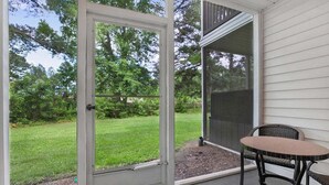 Een overdekt terras met een schuifpui naar een gazon, een ronde tafel en een stoel.