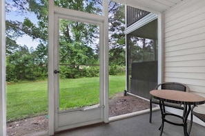 A covered patio with a sliding glass door, a small round table, and a chair. - Fairways 12A (Myrtle Beach)