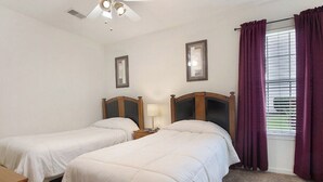 Een slaapkamer met twee enkele bedden, een nachtkastje met een lamp, een plafondventilator en een raam met gordijnen.