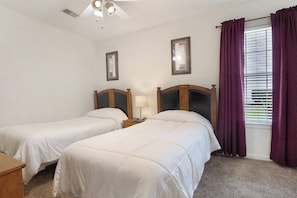 A bedroom with two single beds, a nightstand with a lamp, a ceiling fan, and a window with curtains. - Fairways 12A (Myrtle Beach)