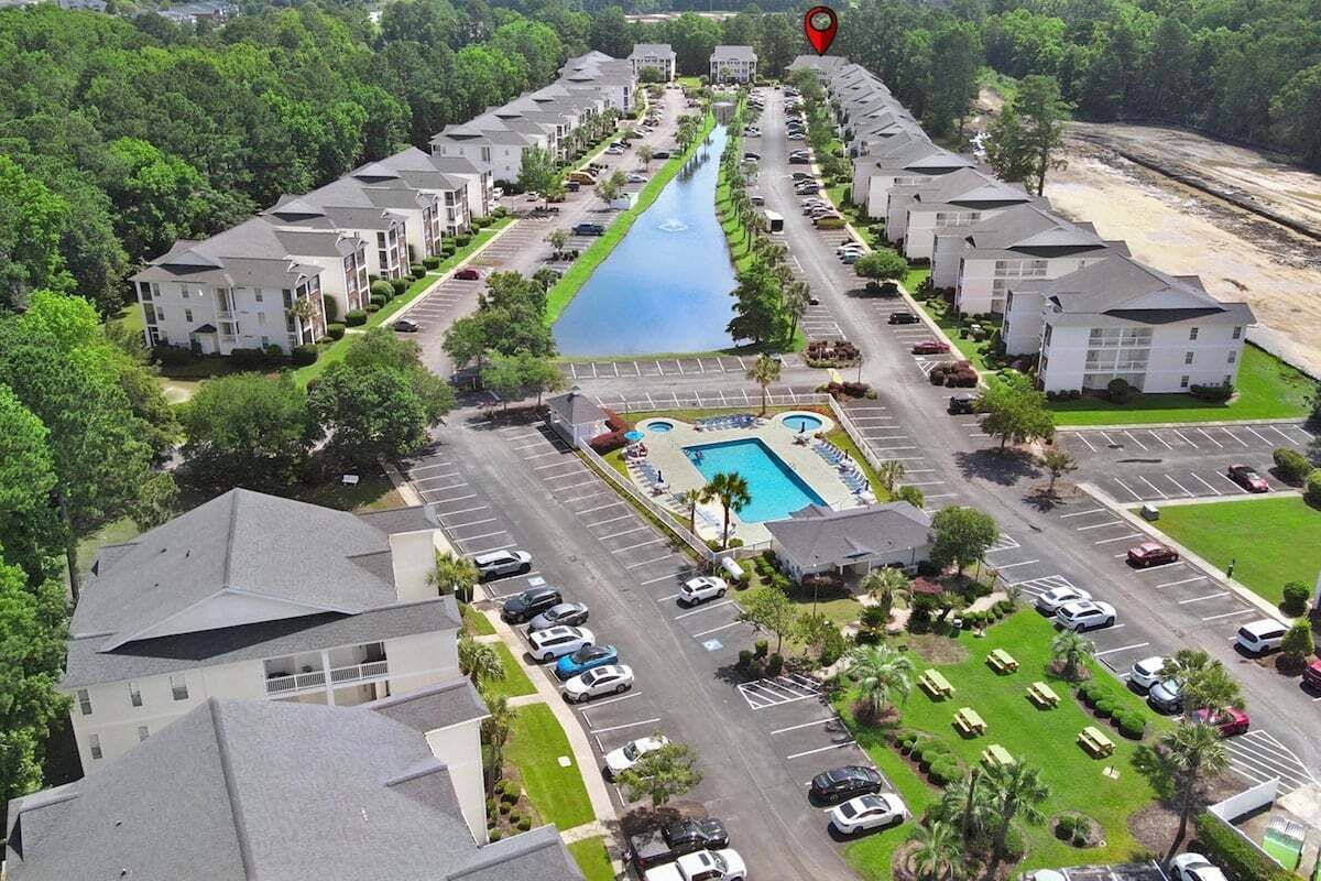 An aerial view of a hotel with a swimming pool, parking lots, and a river running through the property.