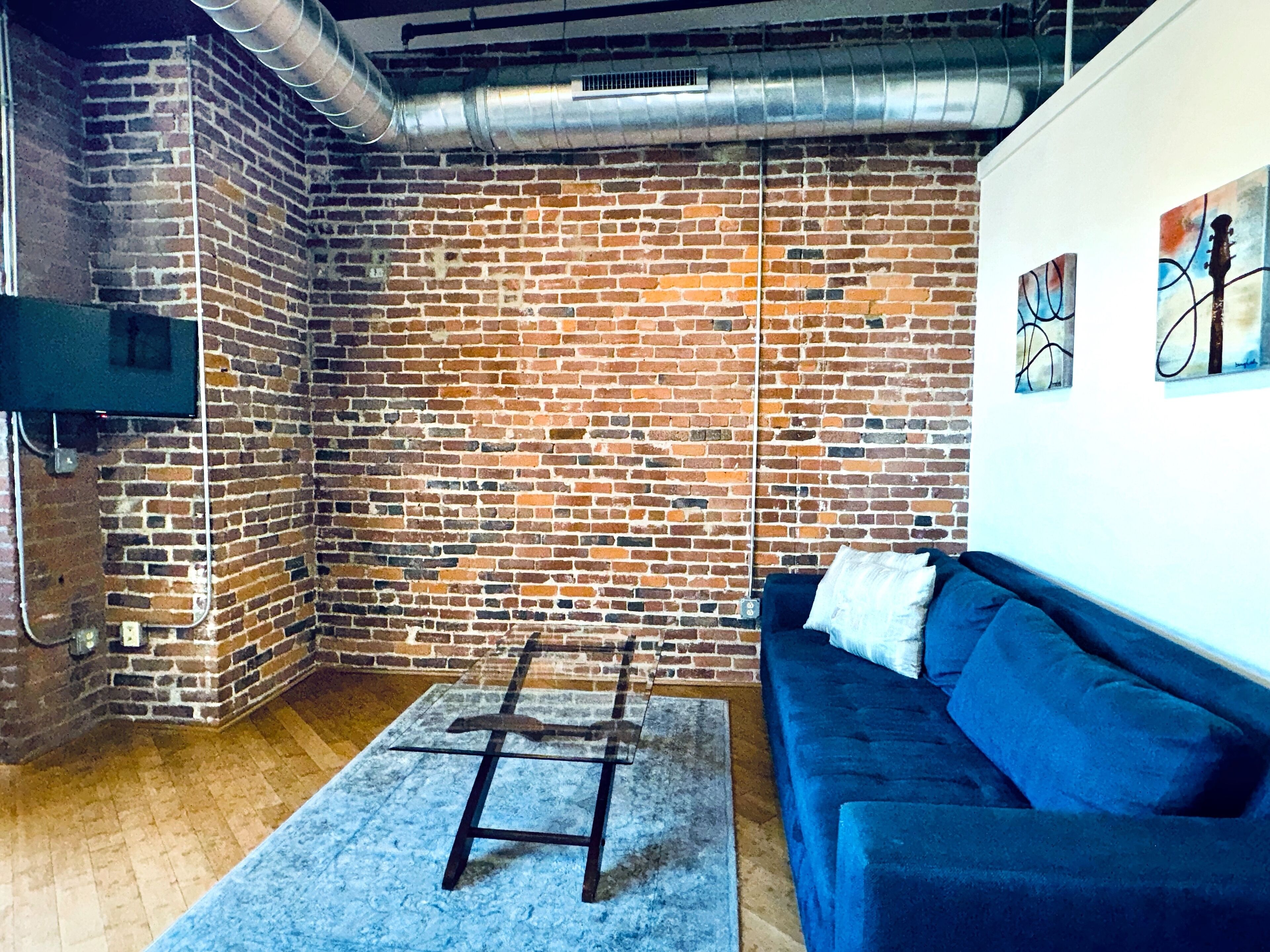 A room with a brick wall, a blue sofa, a glass table, and a mounted TV.