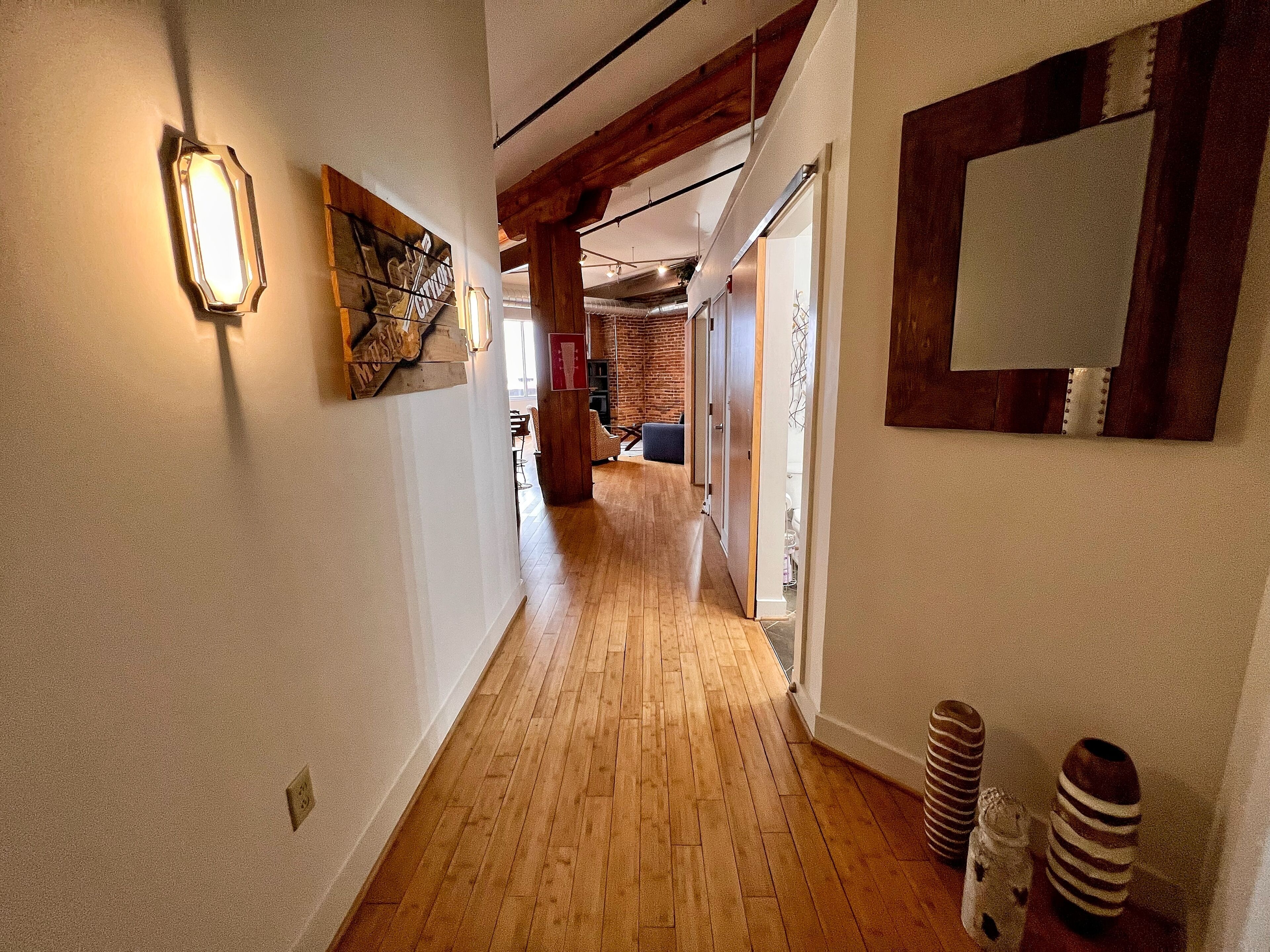 A hallway with wooden flooring, a light fixture, and a framed picture on the wall.