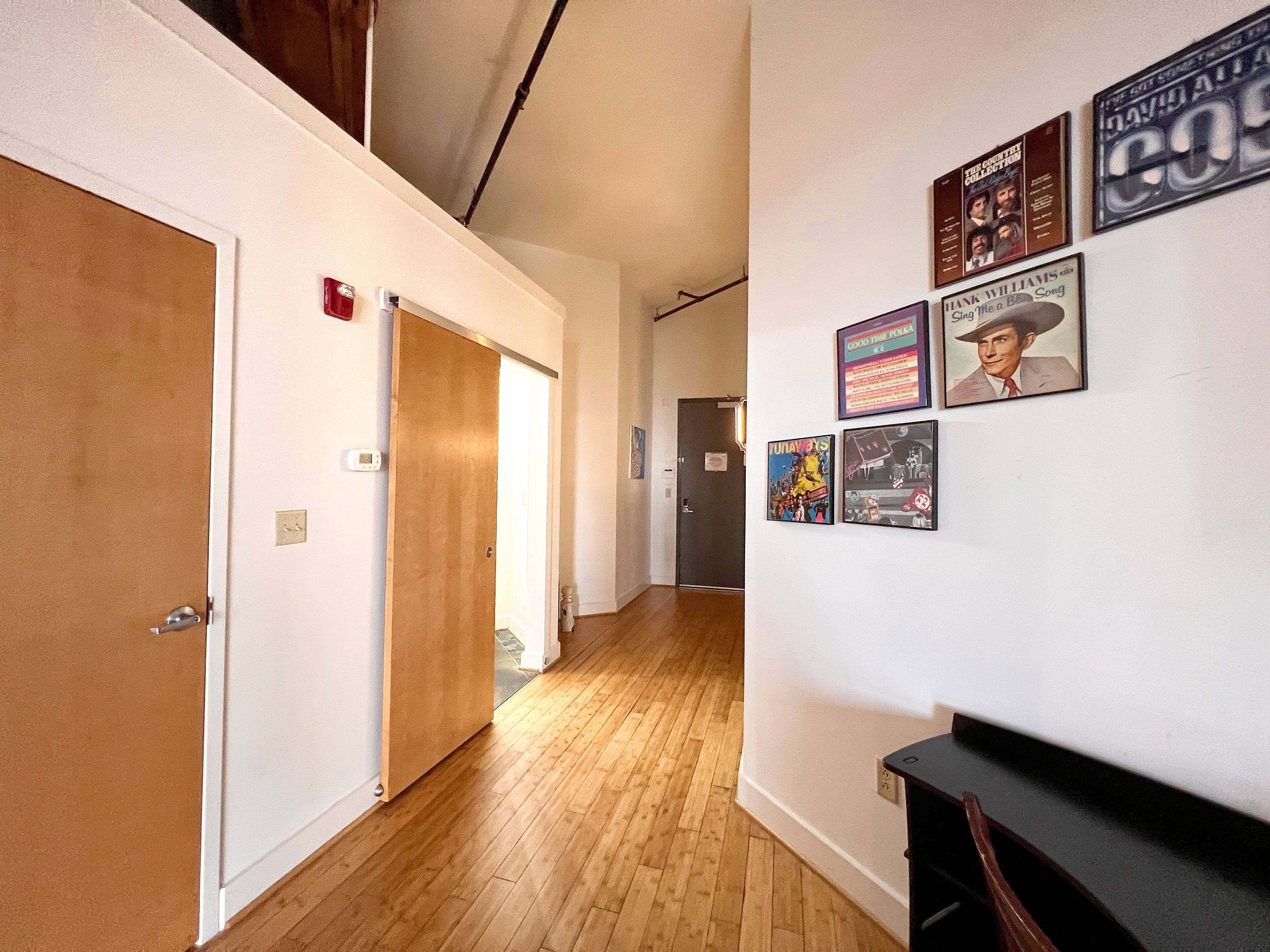 A hallway with wooden flooring, a door, and a wall with framed pictures and a clock.