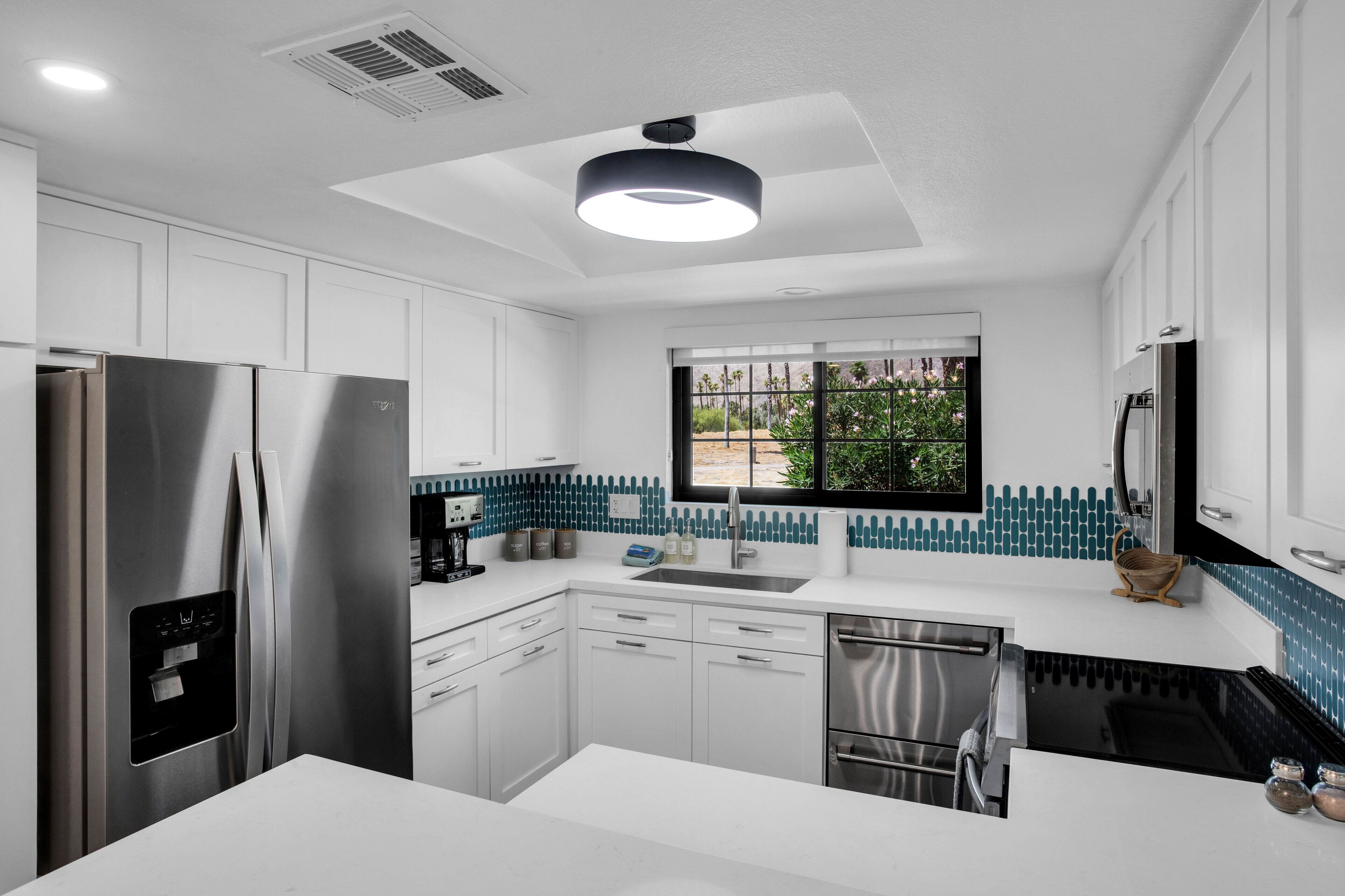 A modern kitchen with white cabinetry, a stainless steel refrigerator, a black stove, and a window with a view of greenery.
