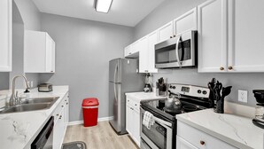 A modern kitchen with white cabinets, stainless steel appliances, a microwave, a refrigerator, a stove, and a sink. - Bf2301-301 (Kissimmee)