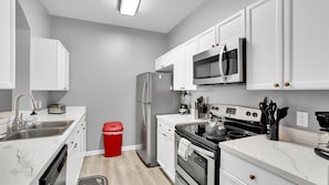 A modern kitchen with white cabinets, stainless steel appliances, a microwave, a refrigerator, a stove, and a sink. - Bf2301-301 (Kissimmee)