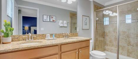 A bathroom with a double sink vanity, a shower enclosure, and a potted cactus.
