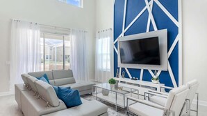 A modern living room with a large flat-screen TV, a sofa set, a coffee table, and a glass-top table. - Wsb610 (Kissimmee)