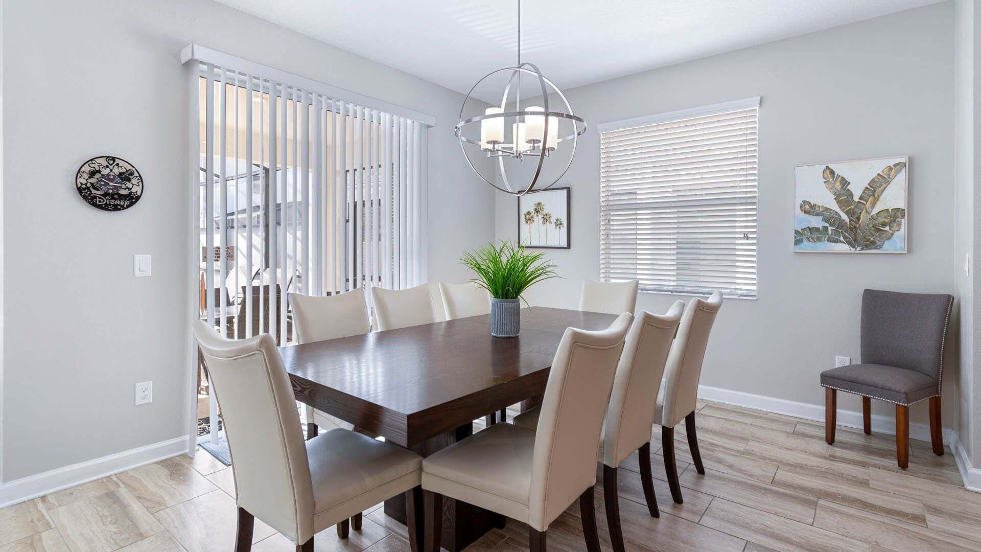 A dining room with a wooden table, six chairs, a potted plant, a chandelier, and artwork on the walls.