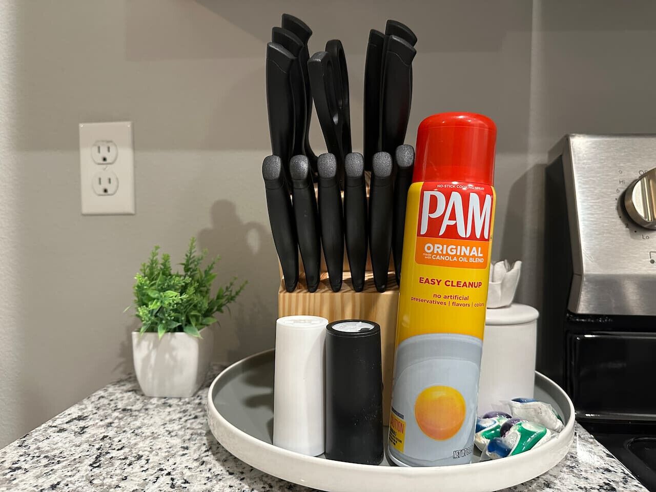 A kitchen counter with a can of PAM Original Canola Oil Blend, a set of black-handled knives, and a white container.
