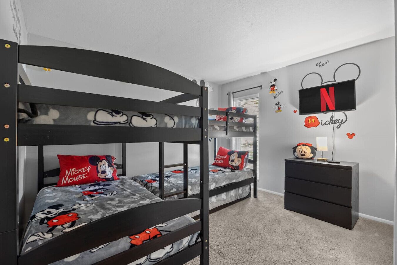 A bunk bed room with Mickey Mouse themed bedding, a TV, and a dresser.