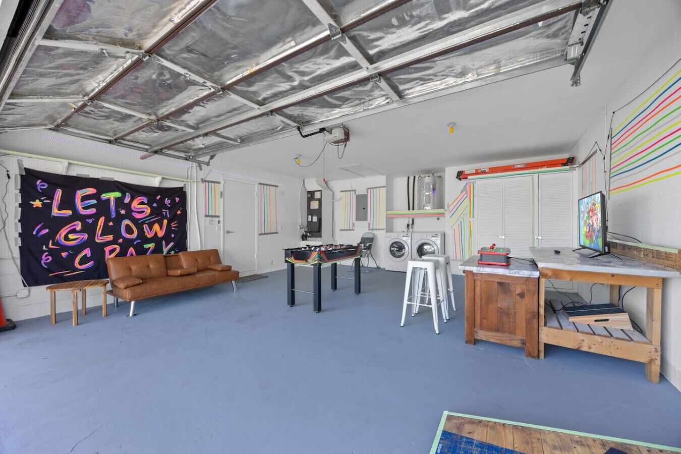 A room with a foosball table, a sofa, a desk with a computer, and a large blackboard with colorful writing.