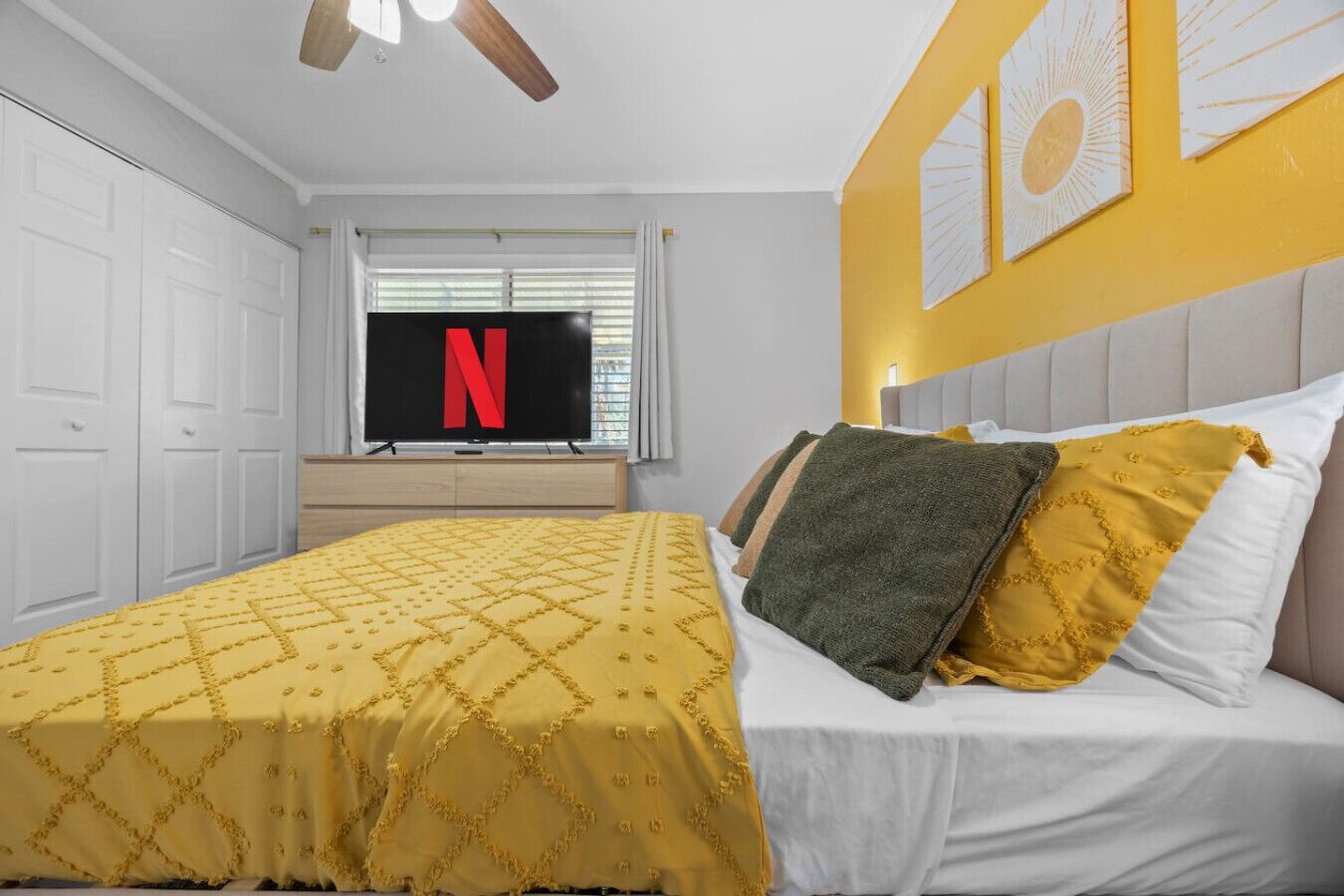 A bedroom with a bed, a TV, and a window with blinds.