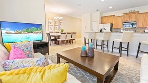 A living room with a TV, sofa, coffee table, and dining area with chairs. - Paradise Palms Resort 4br/3ba Townhome With Splash Pool & Themed Bedrooms (Kissimmee)