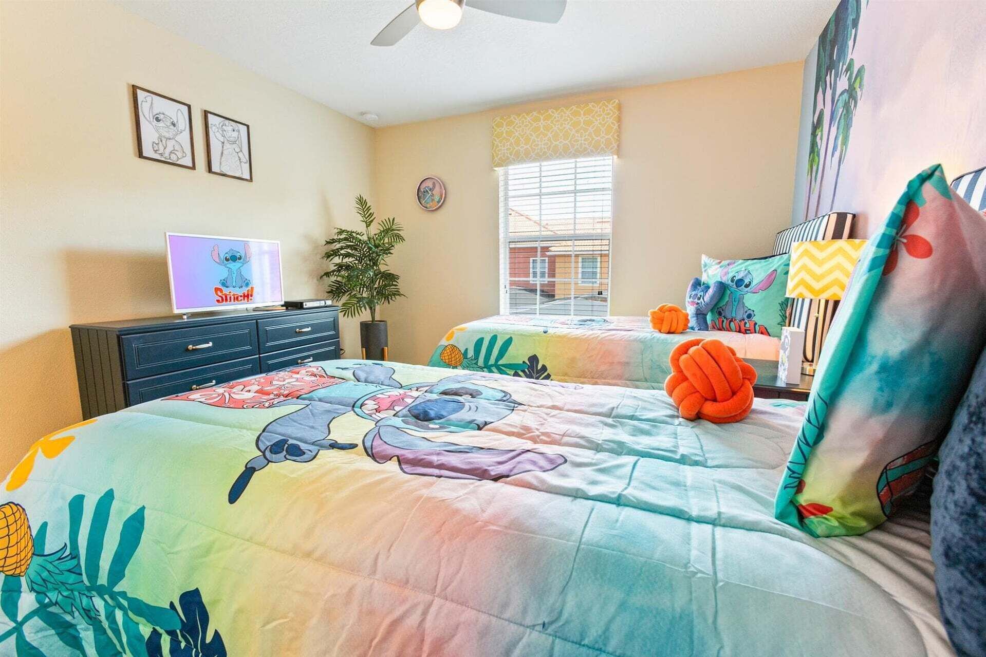 Een slaapkamer met twee bedden, een televisie, een plant en een raam met zonwering.
