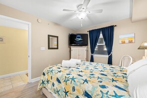 A bedroom with a bed, a ceiling fan, a TV, a window with curtains, and a painting on the wall. - Pelican Isle 112 - Robin`s Nest (Fort Walton Beach)