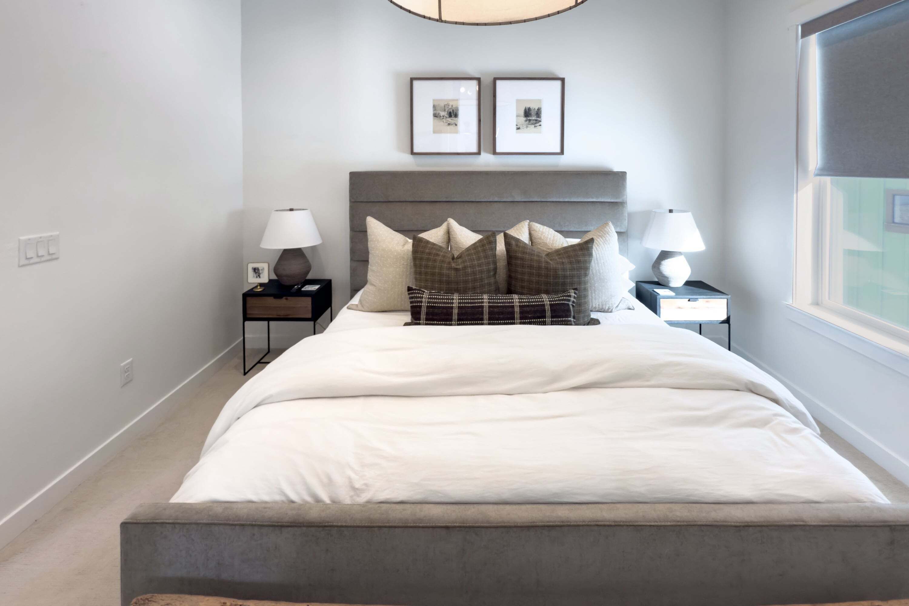 A bedroom with a bed, two bedside tables with lamps, a headboard, and two framed pictures on the wall.