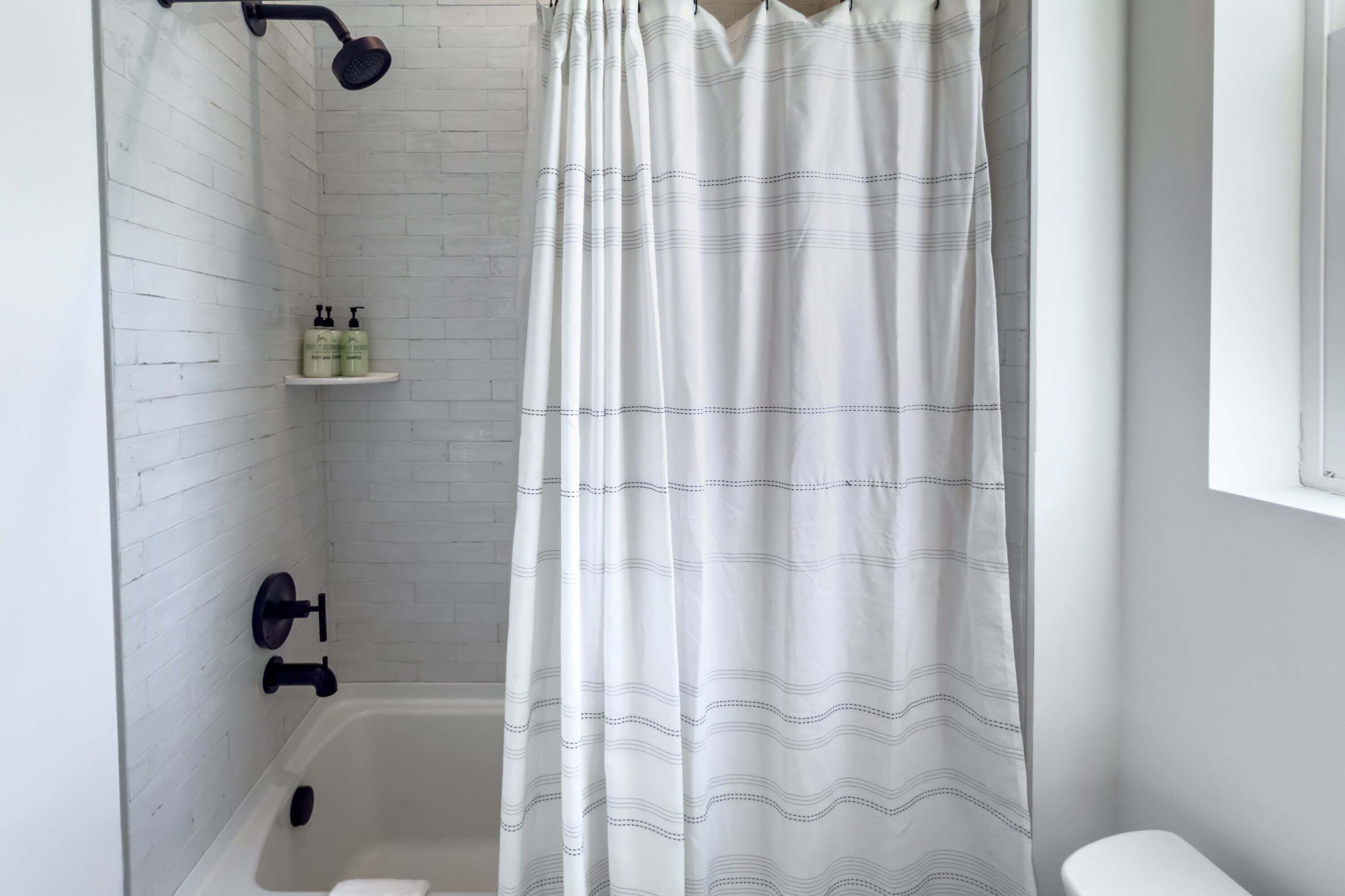 A bathroom with a white shower curtain, a white bathtub, and a white toilet.