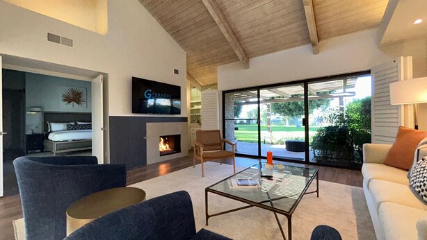 A modern living room with a fireplace, a television, and a glass coffee table. - Racquet Club Retreat (Rancho Mirage)