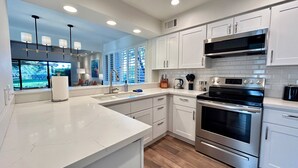 A modern kitchen with white cabinetry, stainless steel appliances, and a large window with blinds. - Racquet Club Retreat (Rancho Mirage)