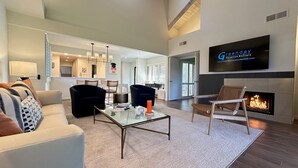 A modern living room with a glass coffee table, black and brown chairs, a fireplace, and a television mounted on the wall. - Racquet Club Retreat (Rancho Mirage)