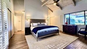 A bedroom with a bed, bedside tables, a dresser, a chair, and a large window. - Racquet Club Retreat (Rancho Mirage)
