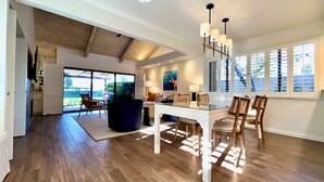 A spacious room with a dining table, chairs, a sofa, and a large window with blinds. - Racquet Club Retreat (Rancho Mirage)