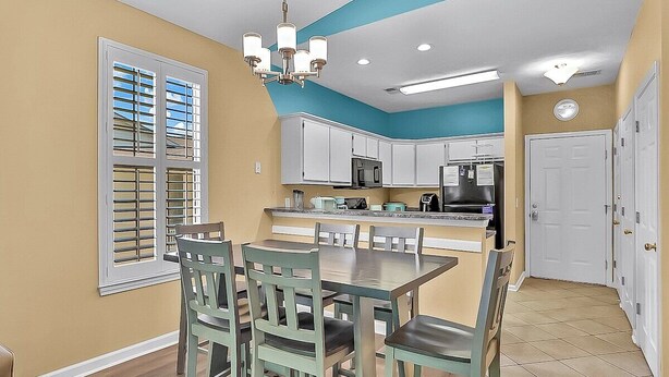 A kitchen with white cabinets, a dining table with chairs, and a blue ceiling. - River Oaks 60N (Myrtle Beach)