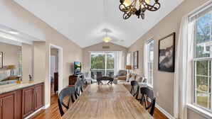 A spacious dining area with a long wooden table, surrounded by chairs, and a kitchen area with wooden cabinets and a countertop. - River Oaks 52I (Myrtle Beach)