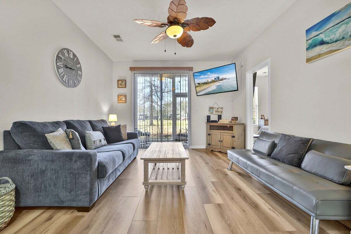 Ein modernes Wohnzimmer mit einem grauen Sofa, einem Holztisch und einem Deckenventilator.