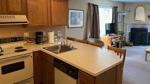 A compact kitchen with wooden cabinets, a built-in oven, a dishwasher, and a central island with a sink. - Pico Village Resort D209 (Killington)