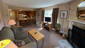 A living room with a sofa, a coffee table, a television, and a fireplace. There is a kitchen in the background. - Pico Village Resort D209 (Killington)
