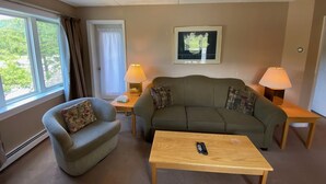 A living room with a sofa, armchair, and coffee table. There are two lamps on side tables, a framed picture on the wall, and a remote control on the table. - Pico Village Resort D209 (Killington)