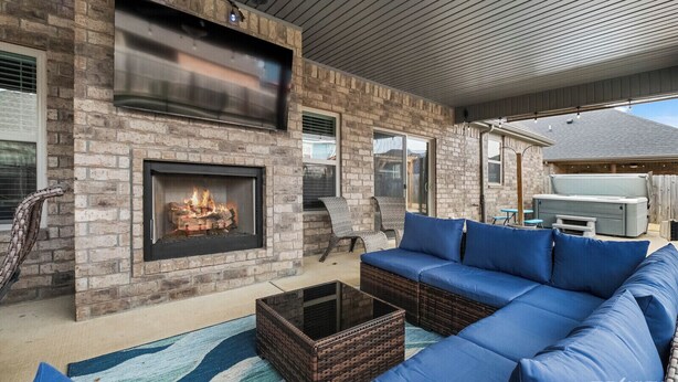 A cozy outdoor living area with a brick fireplace, blue sofa, and a TV mounted on the wall.