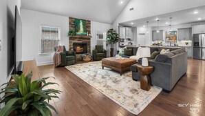 A spacious living room with a fireplace, a large sofa, and a kitchen in the background.