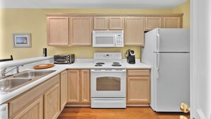 A kitchen with wooden cabinets, a white stove, a microwave, a toaster, and a refrigerator. - River Oaks 7I (Myrtle Beach)