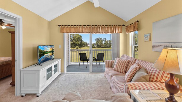 A living room with a TV, a sofa, a lamp, and a ceiling fan. - River Oaks 7I (Myrtle Beach)