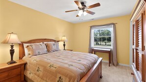 A bedroom with a bed, two bedside tables with lamps, a ceiling fan, a window with curtains, and a view of greenery outside. - River Oaks 7I (Myrtle Beach)