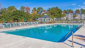 A rectangular swimming pool with a clear blue water surface, surrounded by a concrete deck. There are lounge chairs and umbrellas along the poolside. - River Oaks 7I (Myrtle Beach)
