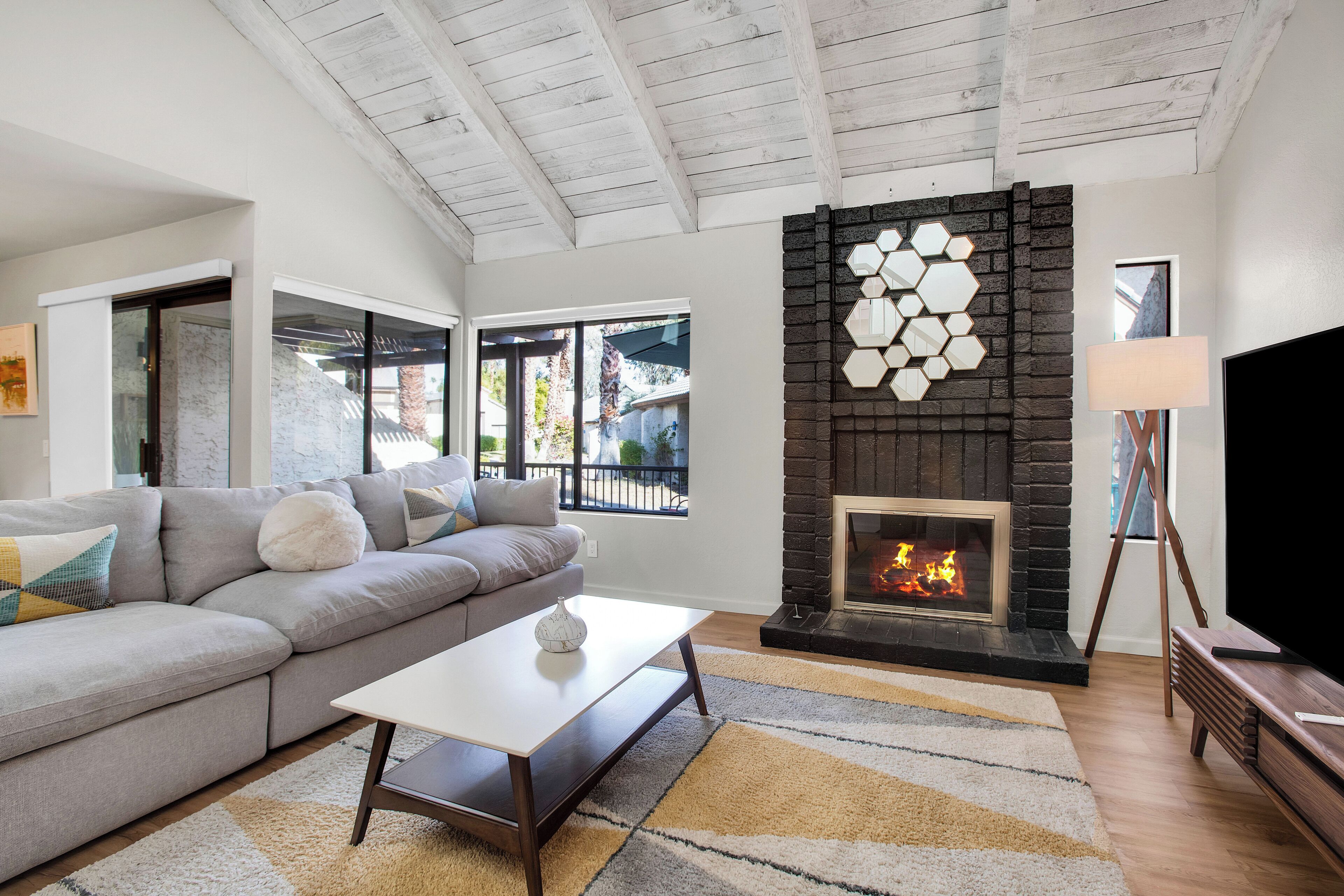 A modern living room with a stone fireplace, a grey sofa, a white coffee table, and a TV on a wooden stand.