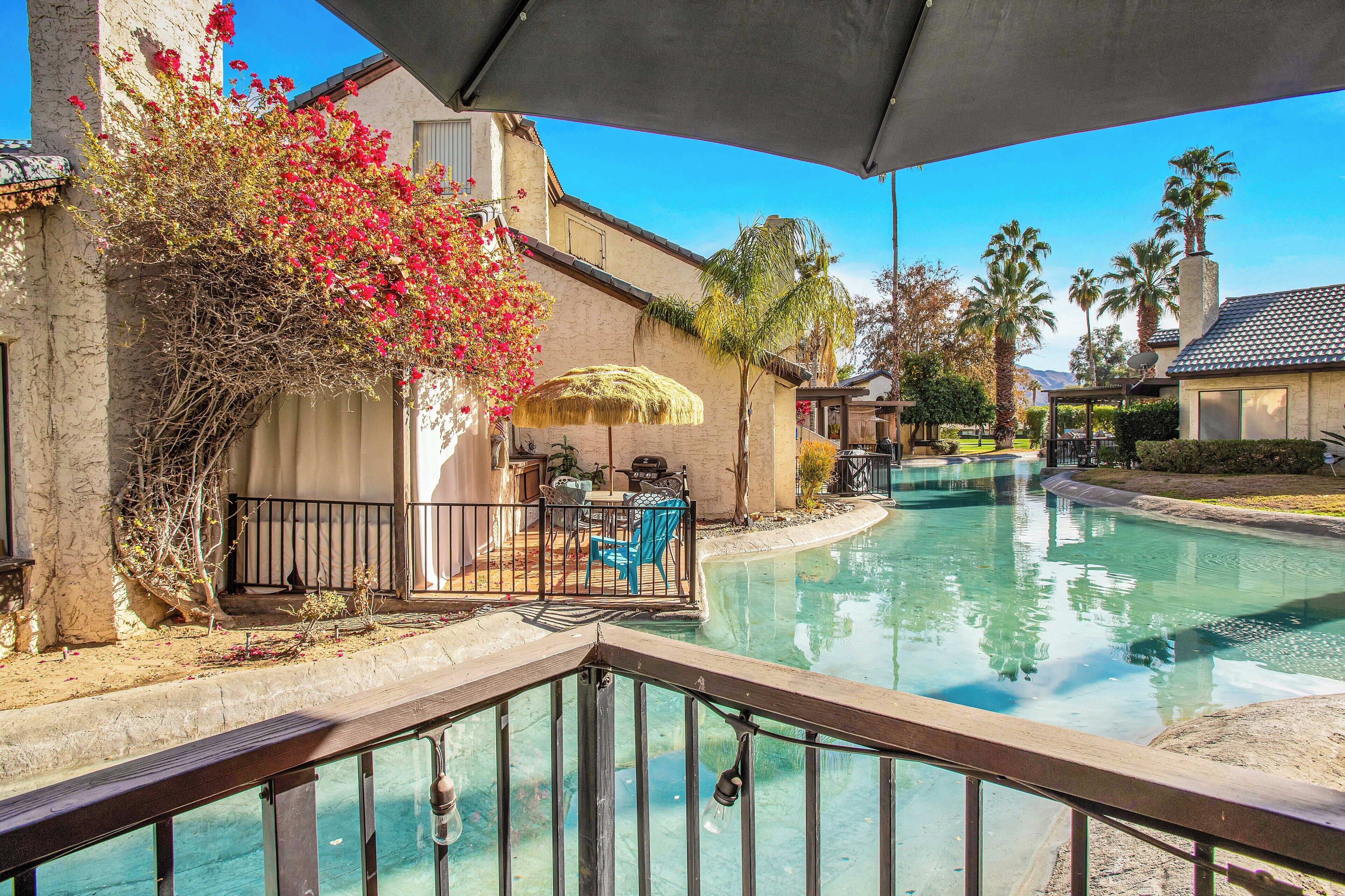 A pool area with a table and chairs, surrounded by a fence and palm trees.